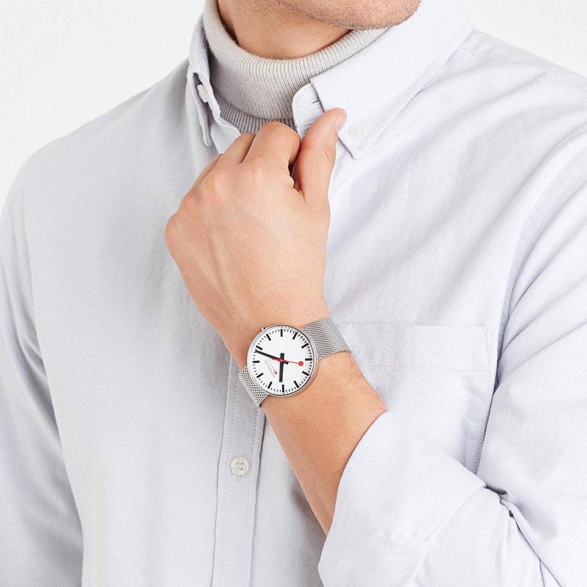 Mondaine Herenhorloge 42mm - Giant MSX.4211B.SM met wit wijzerplaat en rood secondewijzer, gedragen bij een lichtgrijs overhemd. Stijlvol Swiss Made horloge voor heren.