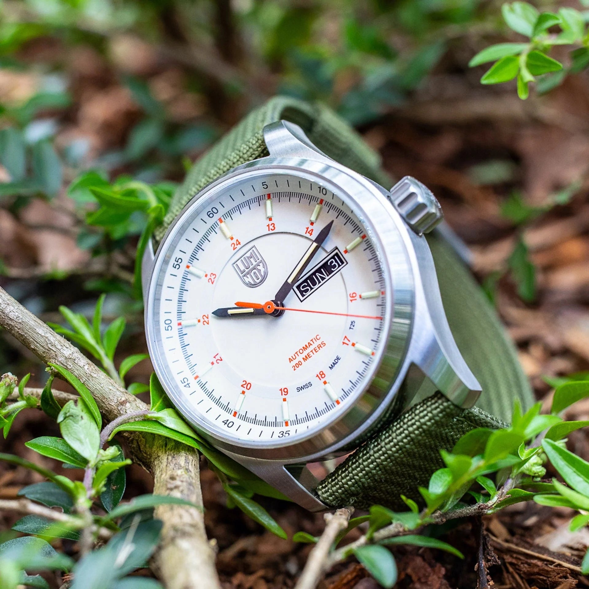 Luminox xl 1907 nf Atacama Field Automatic Herenhorloge 45mm met witte wijzerplaat en groene nylon band, outdoor gepresenteerd tussen bladeren.