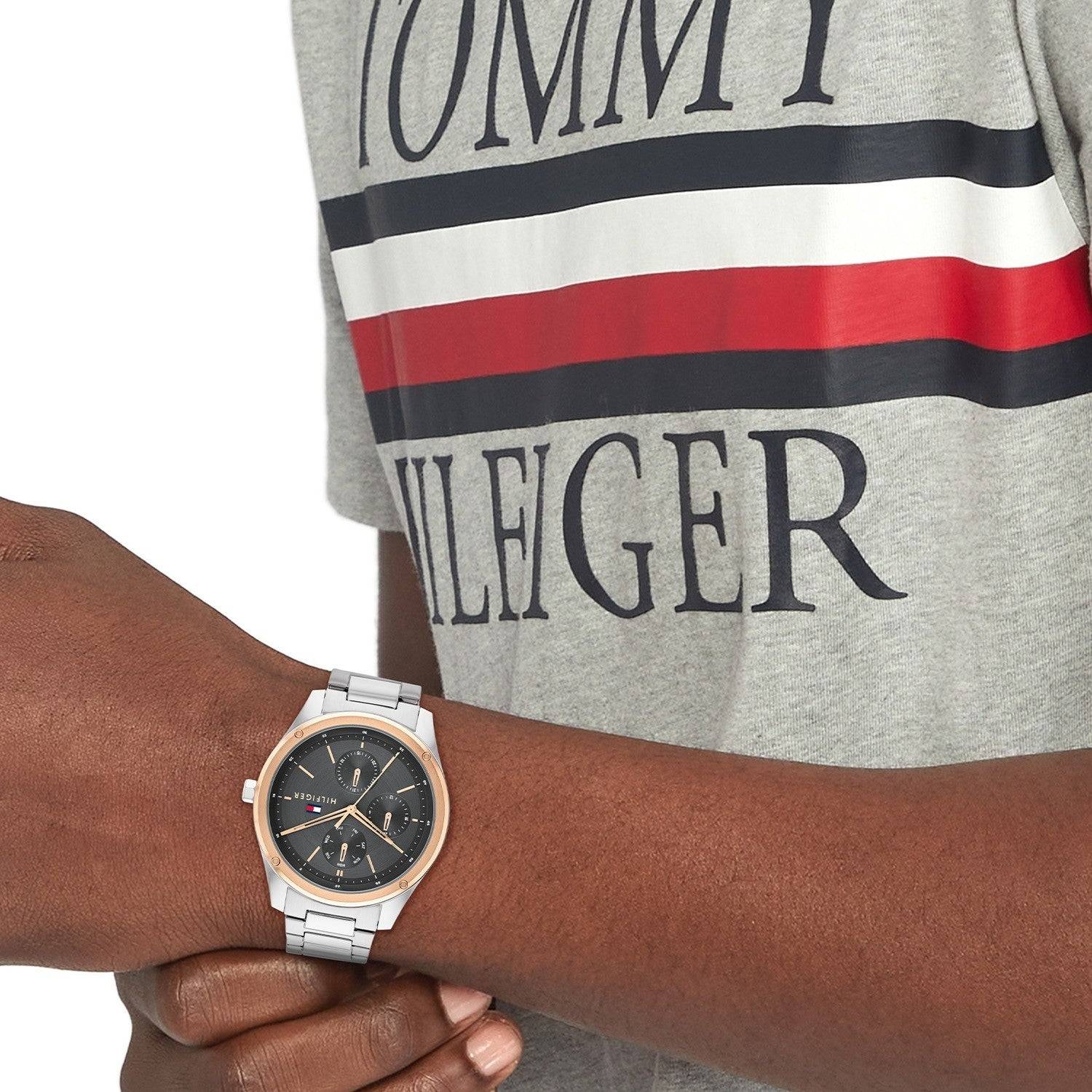 Tommy Hilfiger TH1710541 herenhorloge 43mm met zilverkleurige schakelband en zwarte wijzerplaat, gedragen door man in Tommy Hilfiger shirt. Stijlvol accessoire voor herenmode.